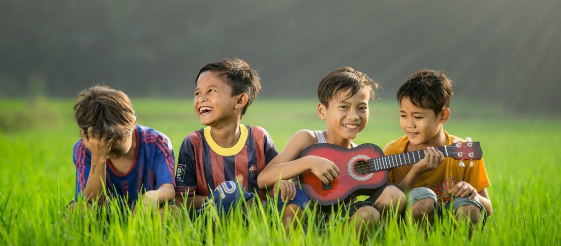 Photo by Robert Collins four boys laughing and sitting on grass during daytime